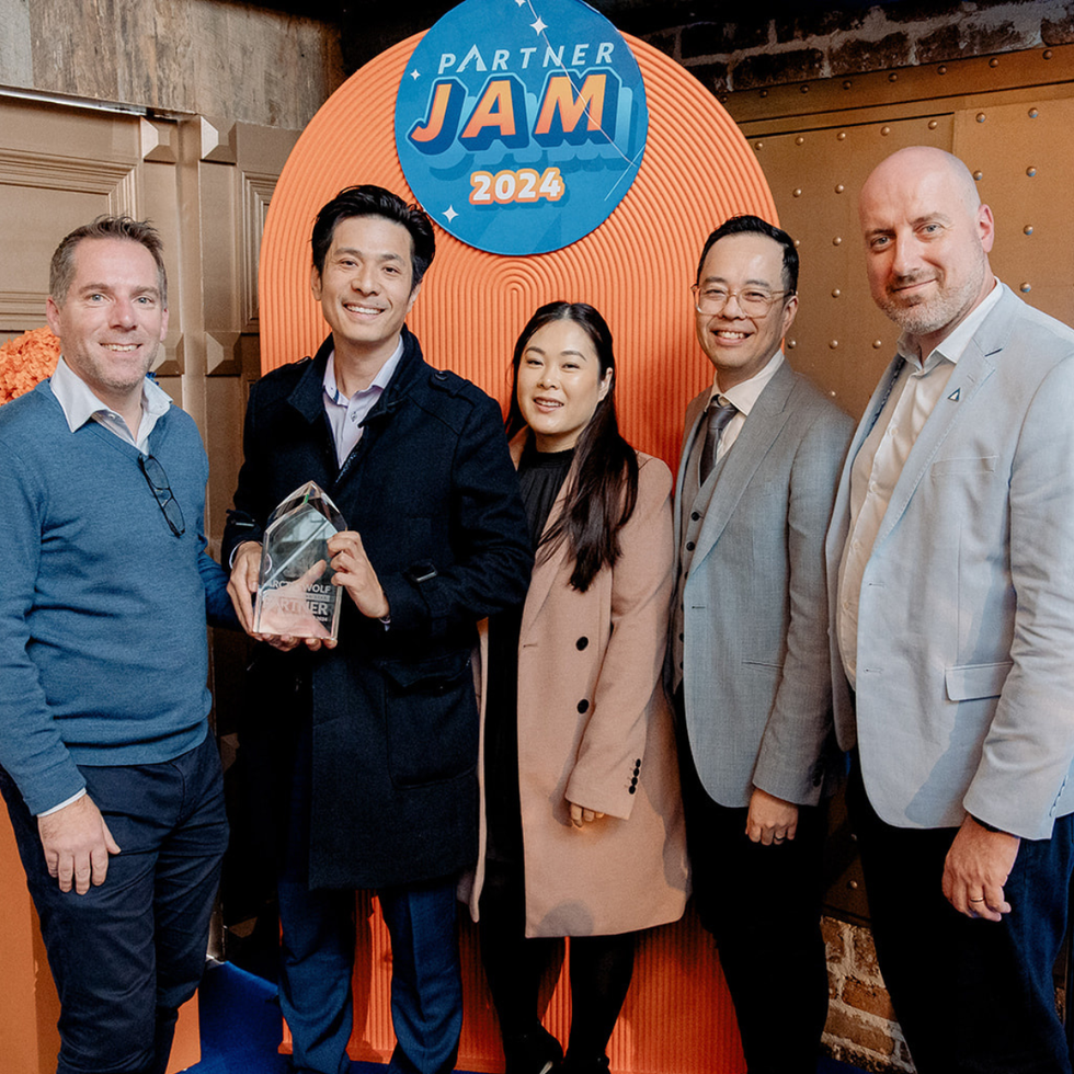 Five people pose, holding an award, in front of a Partner Jam 2024 backdrop; brick wall behind.