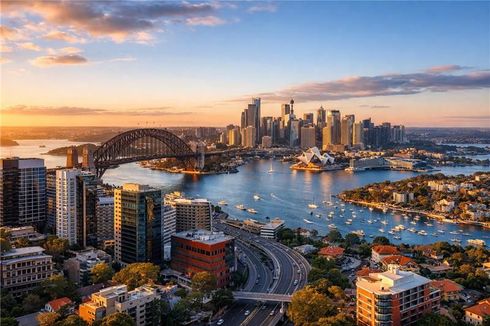 Sydney Harbour at sunset: iconic bridge, skyline, boats on water, and colorful sky.