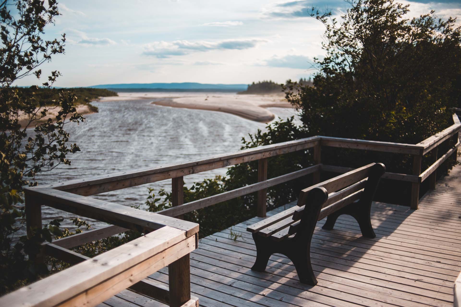 A wooden deck with a bench on it overlooking a body of water