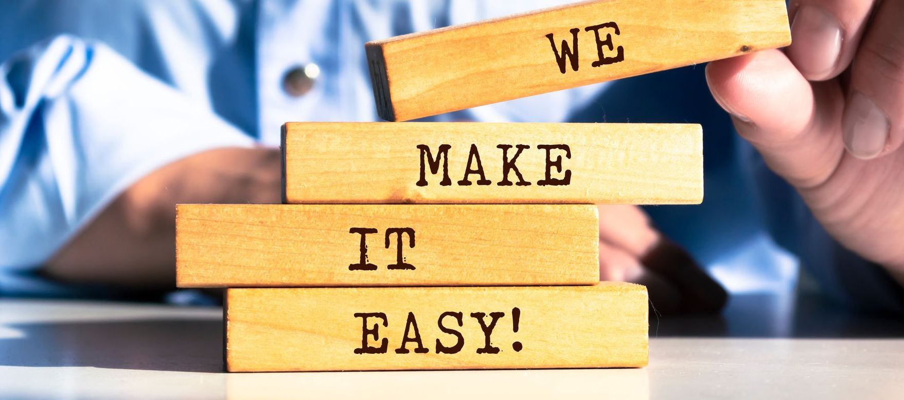 A person is stacking wooden blocks with the words we make it easy written on them.