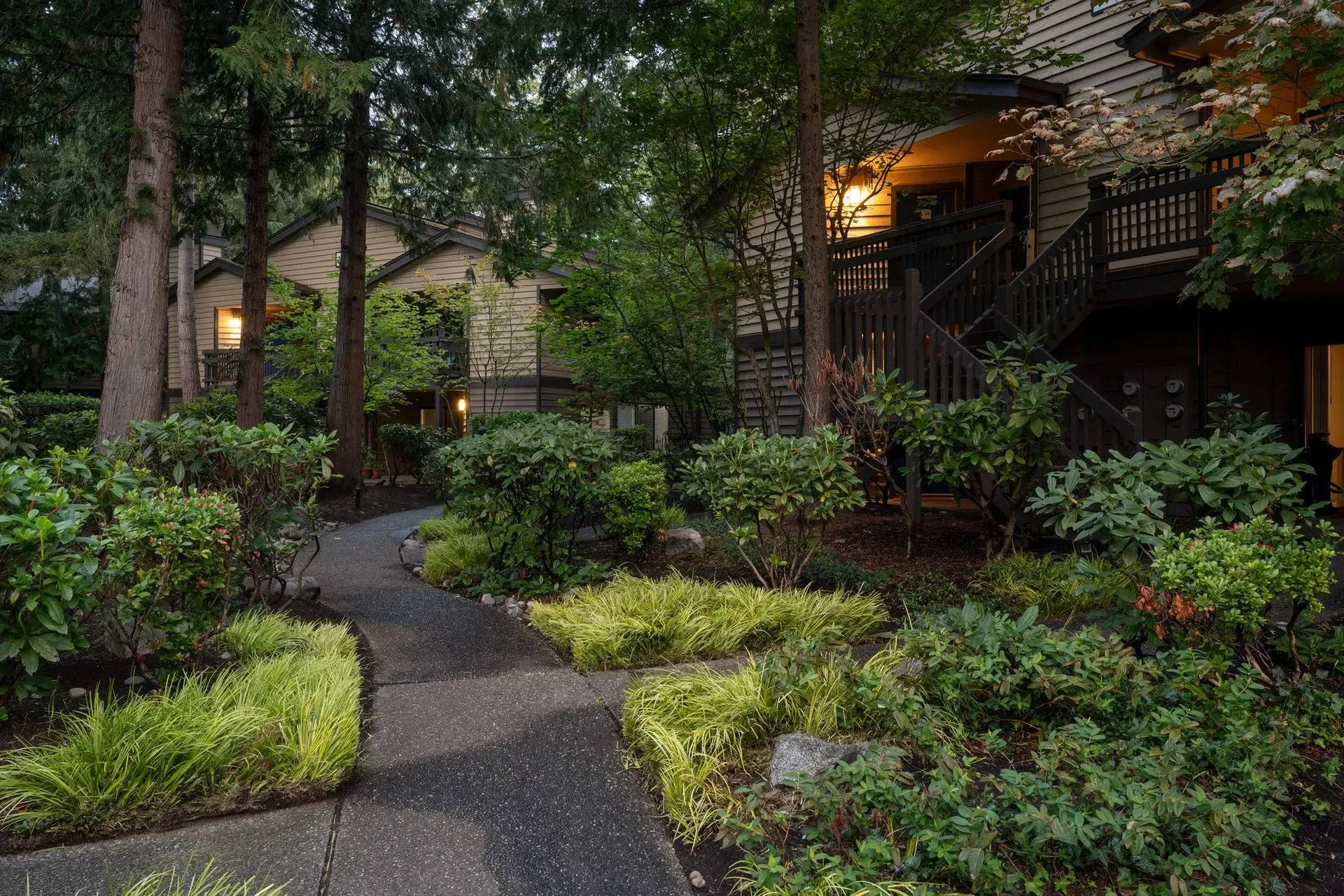 Stone path through lush, green landscaped yard towards building with stairs at Park Bellevue apartment community.