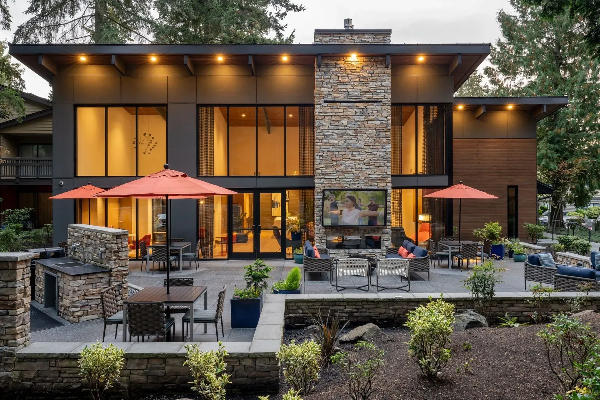 Modern apartment community building at Park Bellevue with a stone facade, outdoor patio, and landscaping; orange umbrellas and seating.