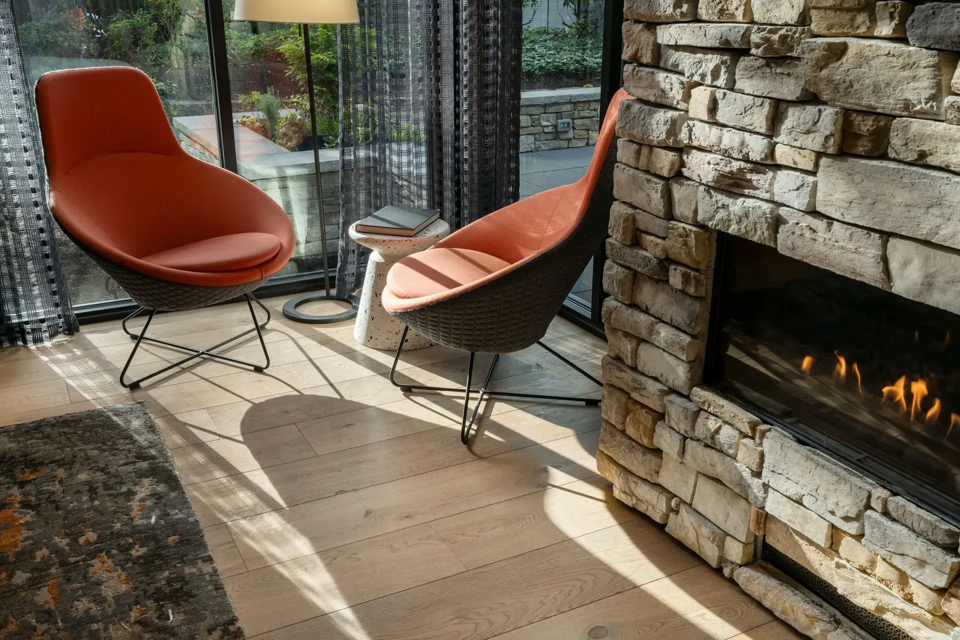 Two orange chairs near a stone fireplace and window at Park Bellevue. Sunlight on wooden floor.