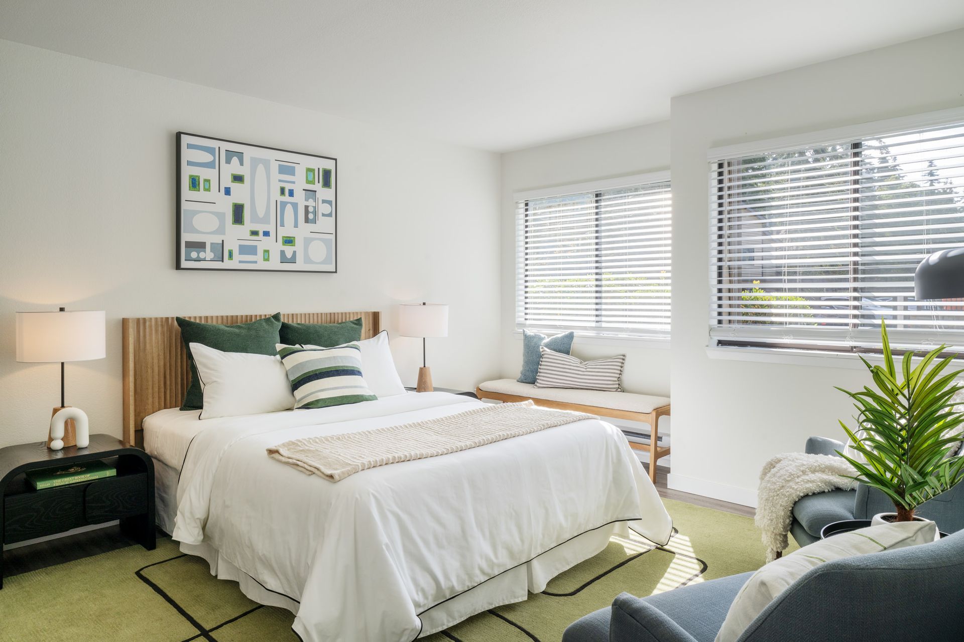 A bedroom with a bed , couch , nightstand , lamp and window.