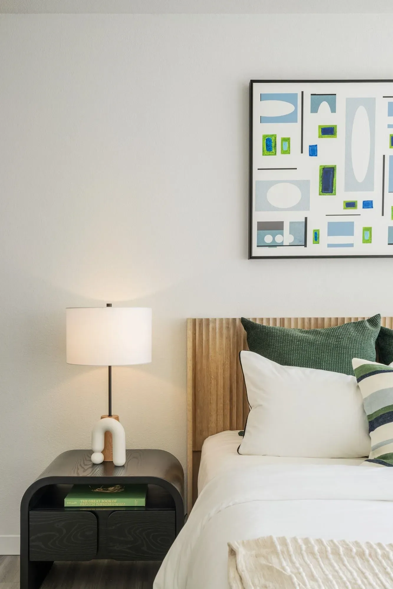 A bedroom with a bed, nightstand, lamp,and painting on the wall.