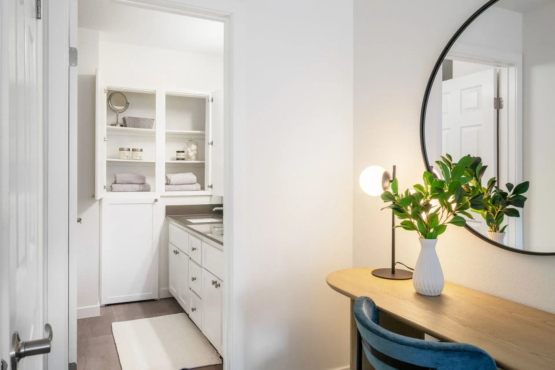 A room with a desk and a bathroom with a mirror in it.