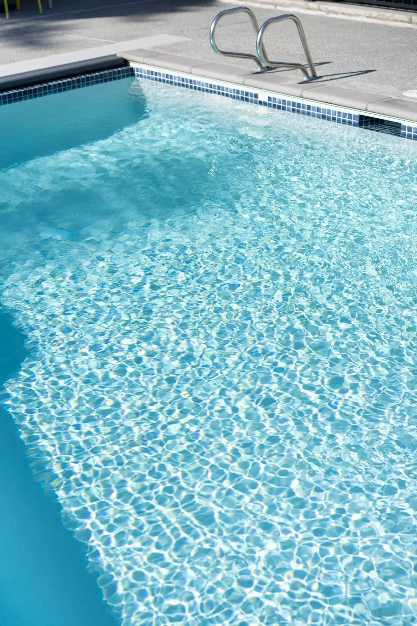 A sparkling blue swimming pool with a metal ladder, viewed on a sunny day at Park Bellevue apartment.