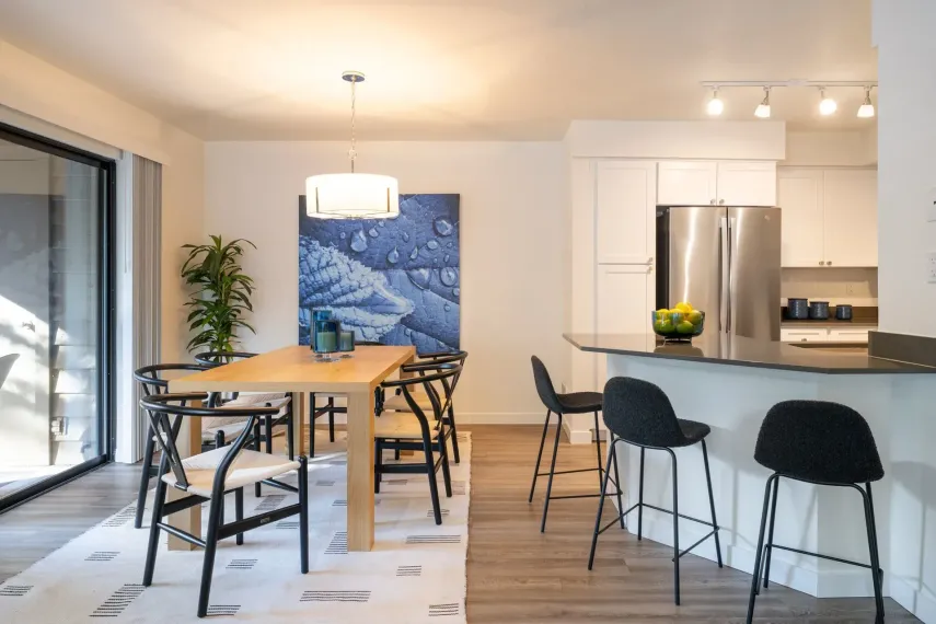 Apartment dining room and kitchen featuring a table, chairs, oversized window, kitchen island, bar chairs, and designer lighting.