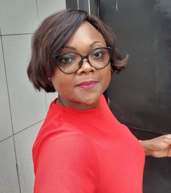 Une femme portant des lunettes et une chemise rouge se tient devant une porte.