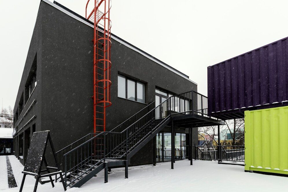 Un bâtiment noir avec des escaliers qui y mènent et une échelle rouge.