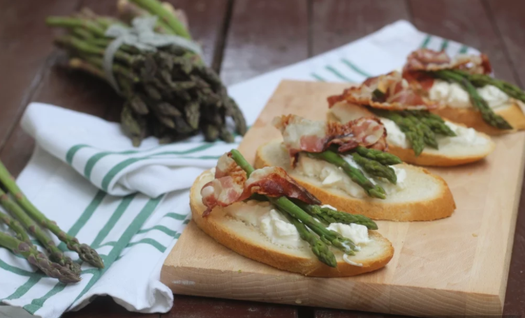 un tagliere di legno condito con asparagi e pancetta su un tavolo.