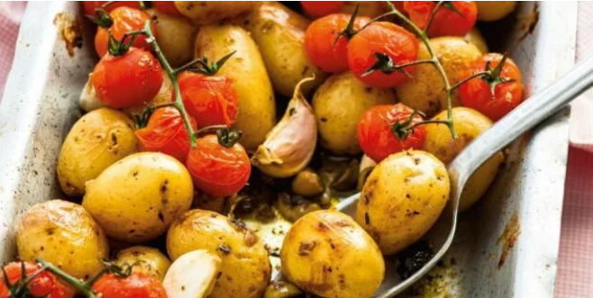 una casseruola piena di patate e pomodori con dentro un cucchiaio.
