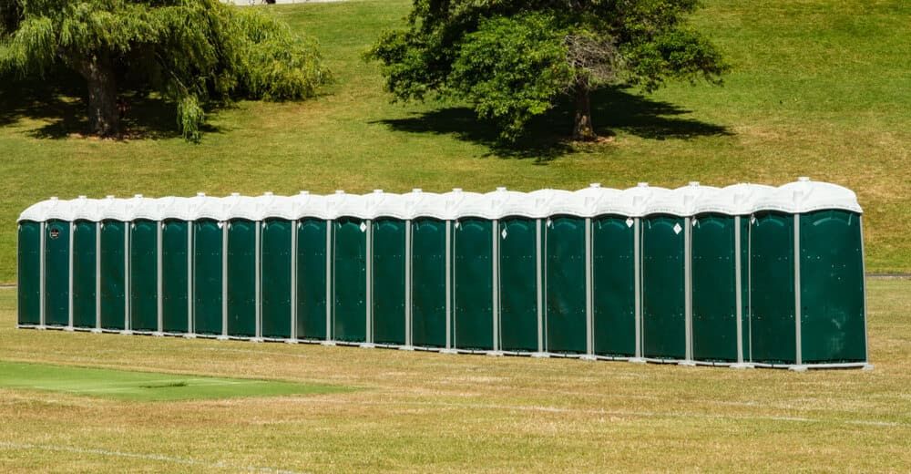 A Row of Green Portable Toilets Are Lined Up in a Grassy Field — Tony Gordon Septic Tank Cleaning in Newee Creek, NSW