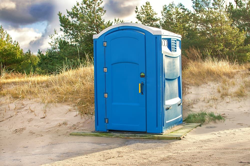A Blue Portable Toilet is Sitting in the Middle of a Field — Tony Gordon Septic Tank Cleaning in Bellingen, NSW