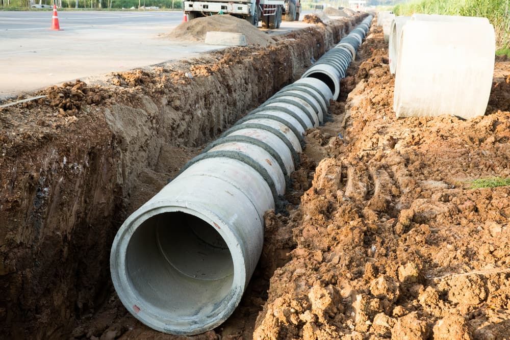 A Concrete Pipe is Being Installed in a Trench Next to a Road — Tony Gordon Septic Tank Cleaning in Coffs Harbour, NSW