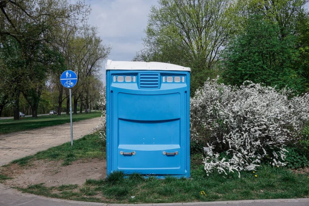 A Blue Portable Toilet is Sitting on the Side of the Road in a Park — Tony Gordon Septic Tank Cleaning in Kempsey, NSW
