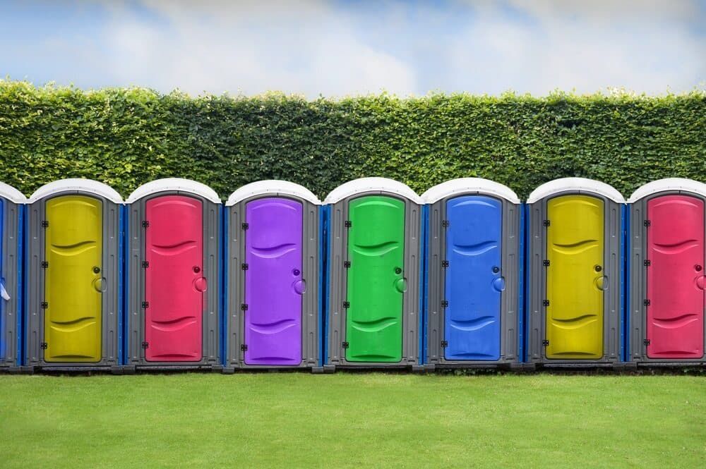 A Row of Colorful Portable Toilets Are Lined Up in a Grassy Field — Tony Gordon Septic Tank Cleaning in Newee Creek, NSW