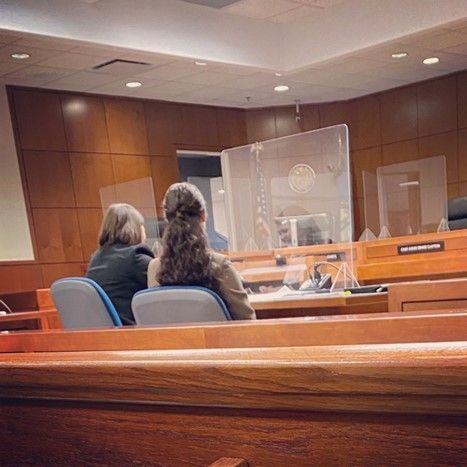 Two women are sitting in a courtroom in front of a screen.
