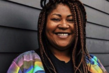 A woman with braids is smiling in front of a black wall
