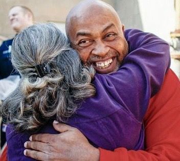 A man in a red shirt is hugging a woman in a purple shirt.