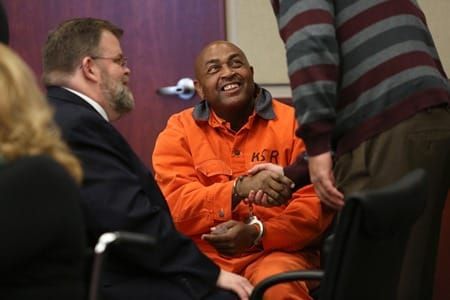 A man in an orange jumpsuit is shaking hands with a man in a suit.