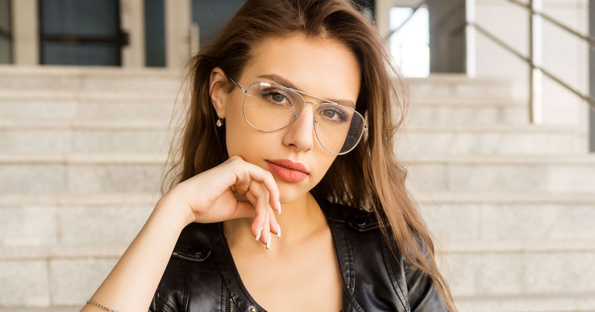 A woman wearing oversized aviator glasses and a leather jacket is standing on a set of stairs.