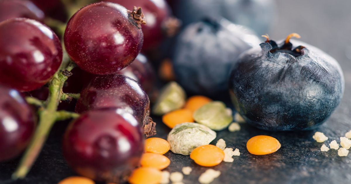 Close-up of red grapes and blueberries with orange and green lentils on a dark surface.