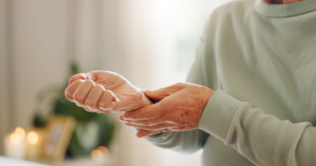 A person in a light green long-sleeved shirt gently holds their wrist, suggesting pain or discomfort.