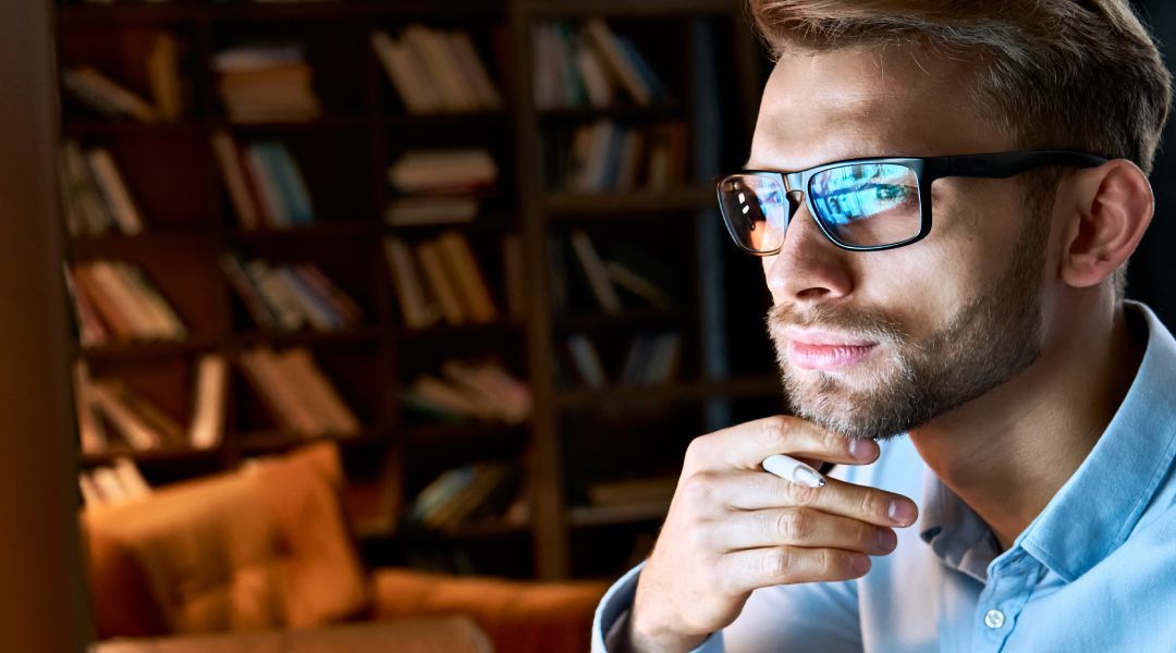 A man wearing glasses is sitting in front of a computer screen
