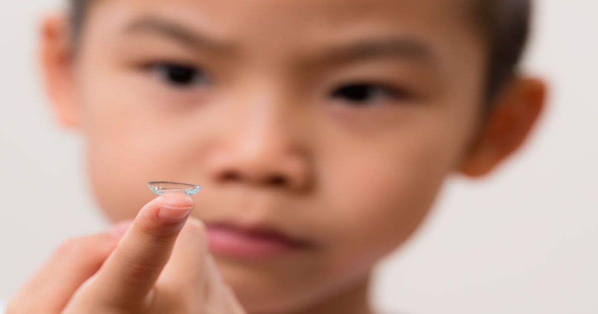 A young child is holding a contact lens on their finger.