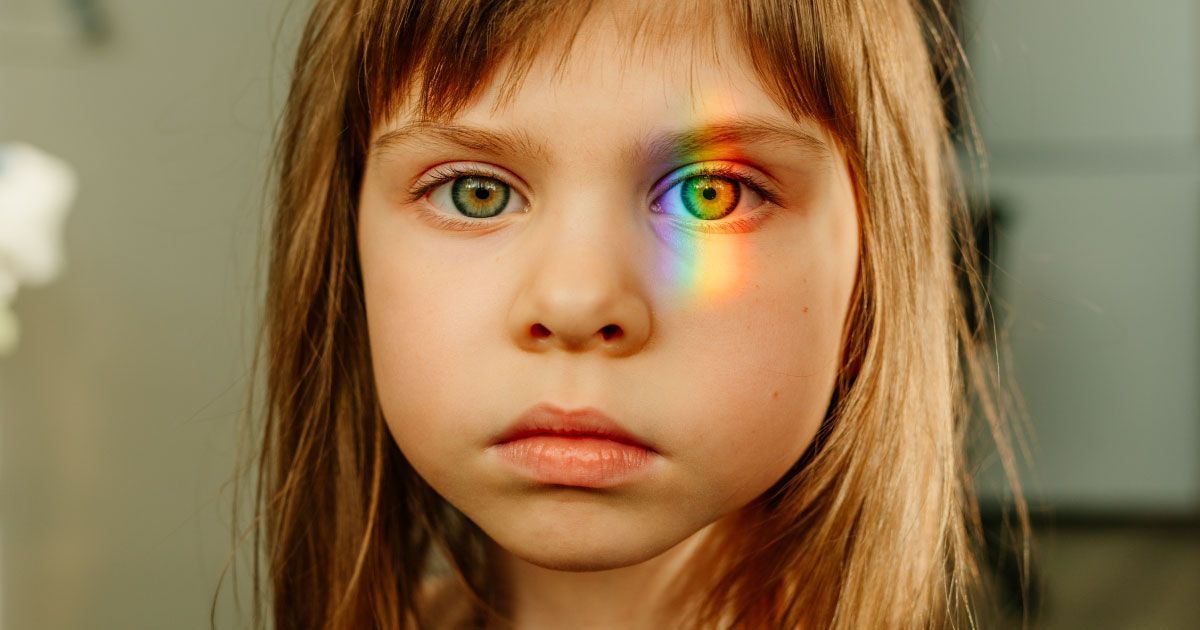 A little girl with a rainbow reflected in her left eye.