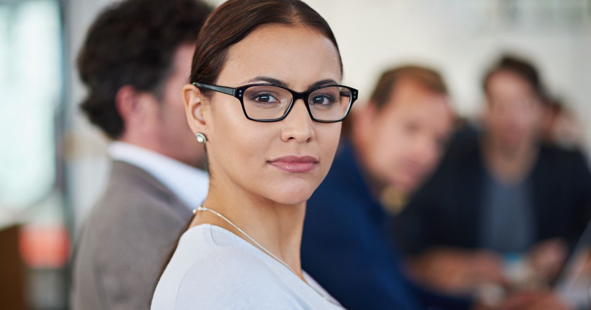 A woman wearing glasses is standing in front of a group of people.