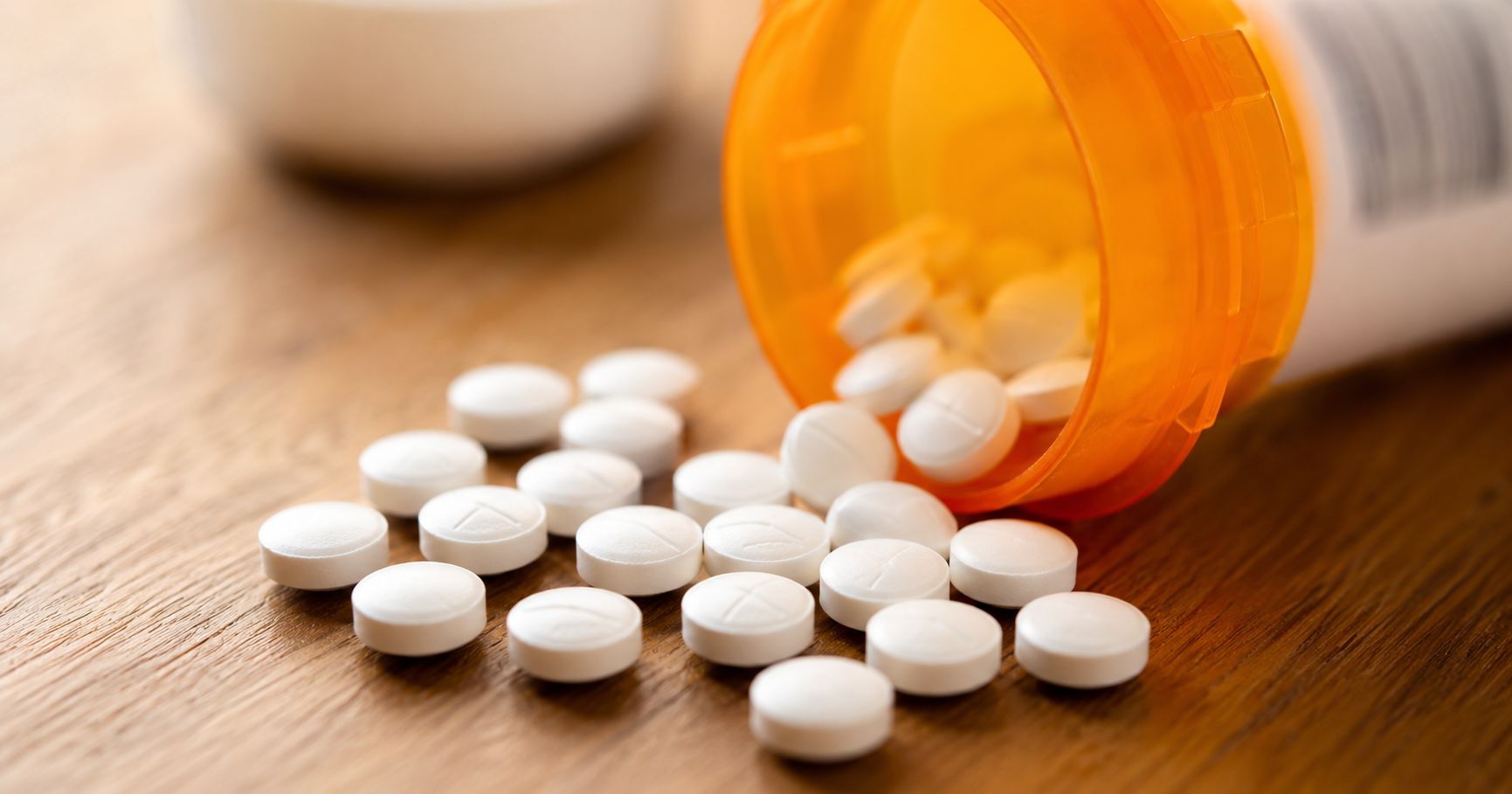 Orange prescription bottle with white pills spilled onto a wooden surface