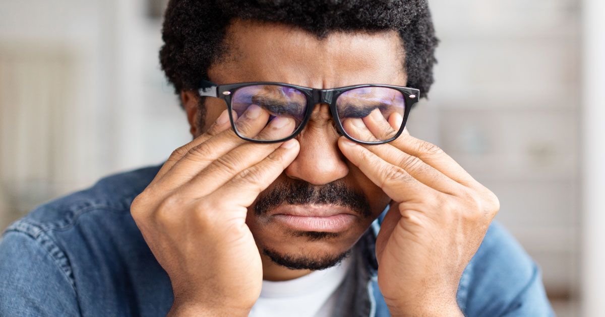 A man with glasses is holding his cheek from tooth pain.