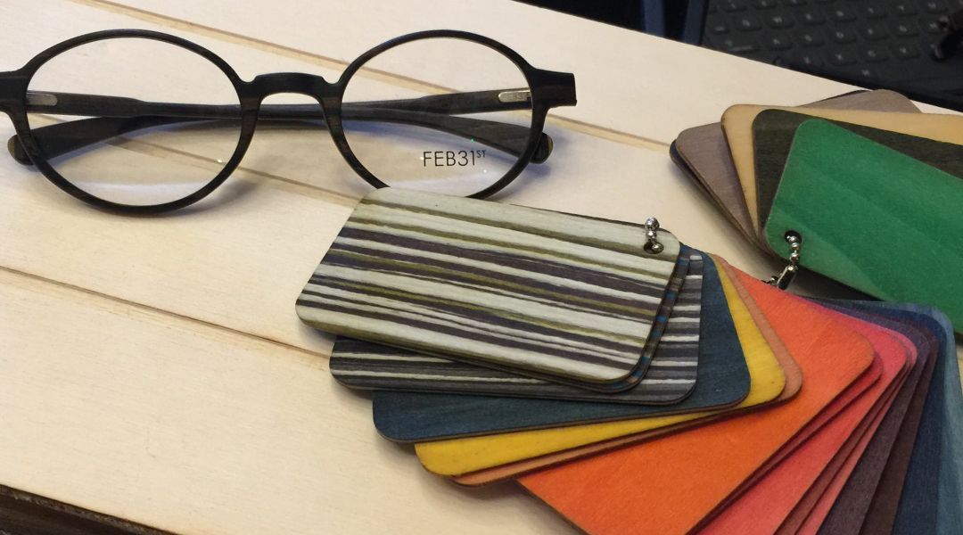 A pair of wood-framed glasses sitting on top of a wooden table with colorful wood sample chips.