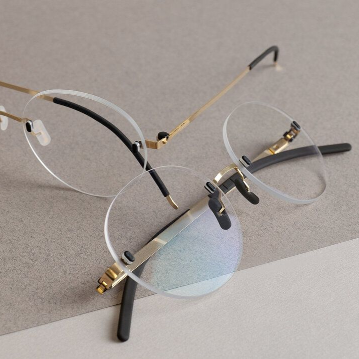 Two Gotti rimless eyeglasses with round lenses laid on a gray surface