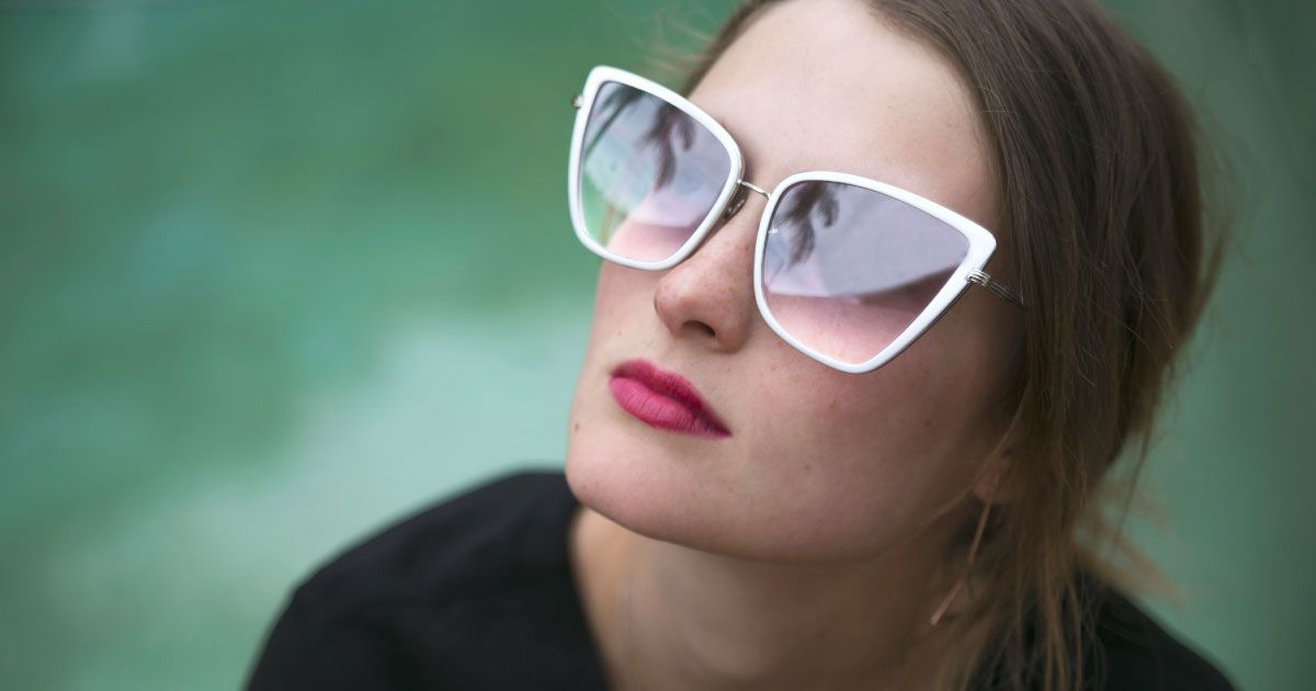 A woman wearing sunglasses with grey gradient lenses is looking up.