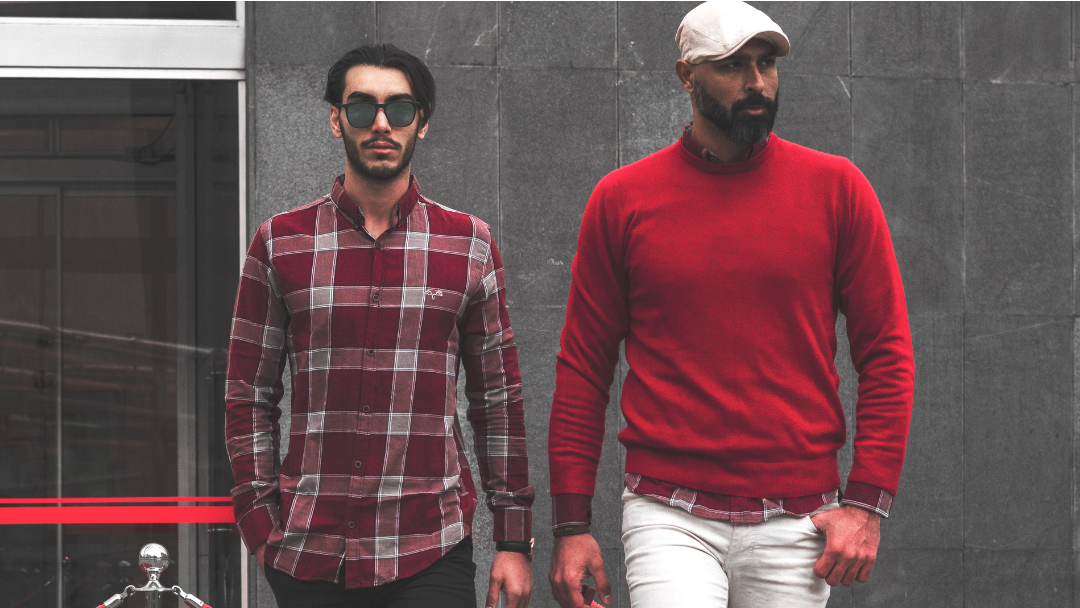 Two men are walking down the street - one wearing a red sweater and the other has sunglasses on