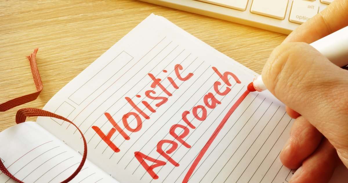 A person is writing in a notebook that says holistic approach