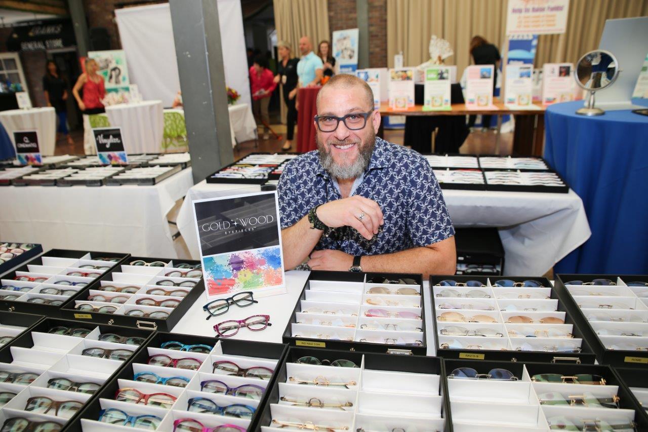 Gold and Wood vendor sitting behind tabletop eyewear display at 2018 Raise Your Glasses