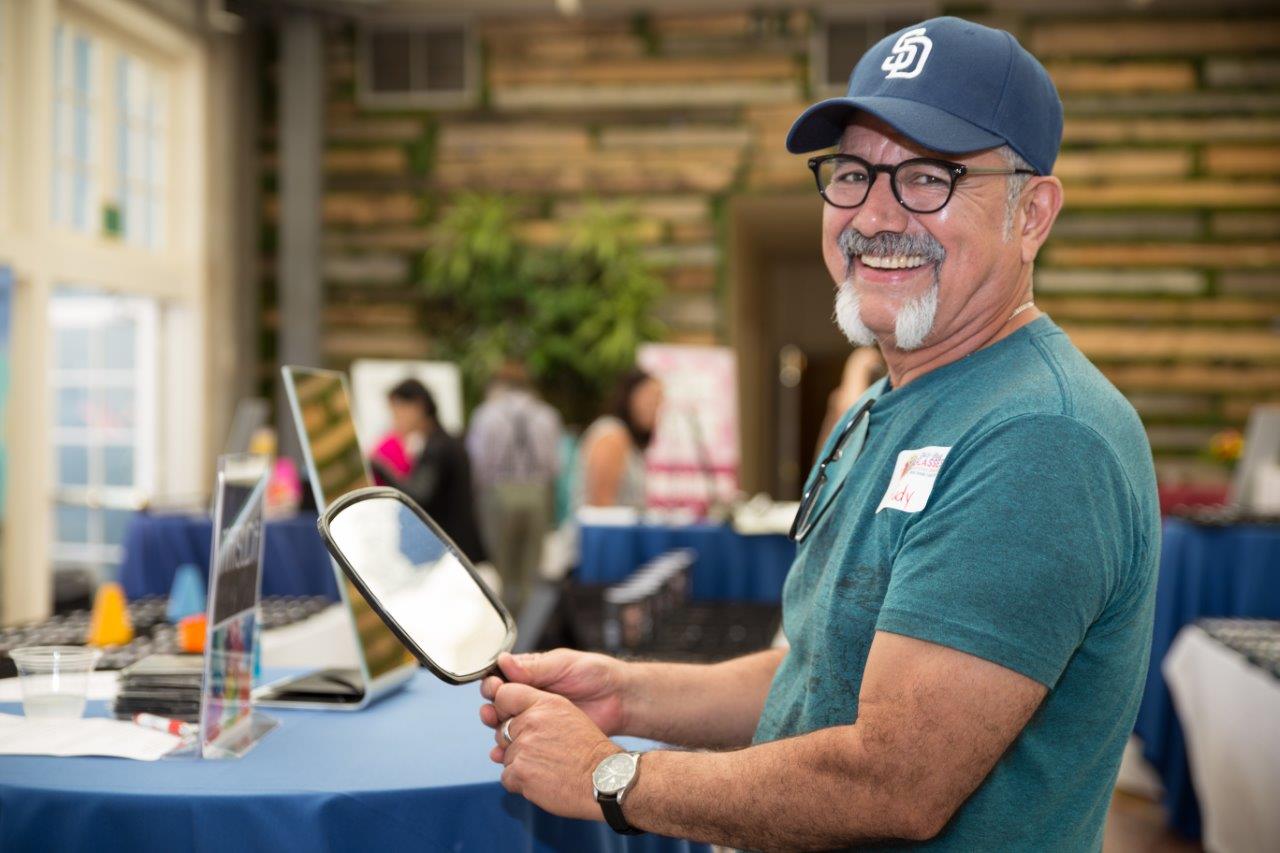Smiling man looking in mirror and trying on glasses at 2018 Raise Your Glasses