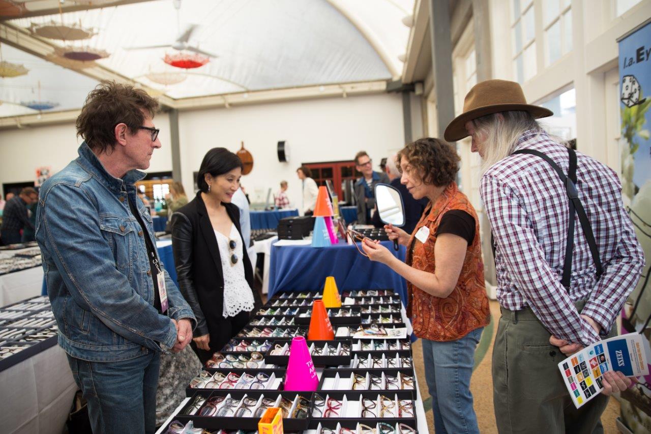 People standing near display boxes of sunglass frames at Raise Your Glasses 2018 Event