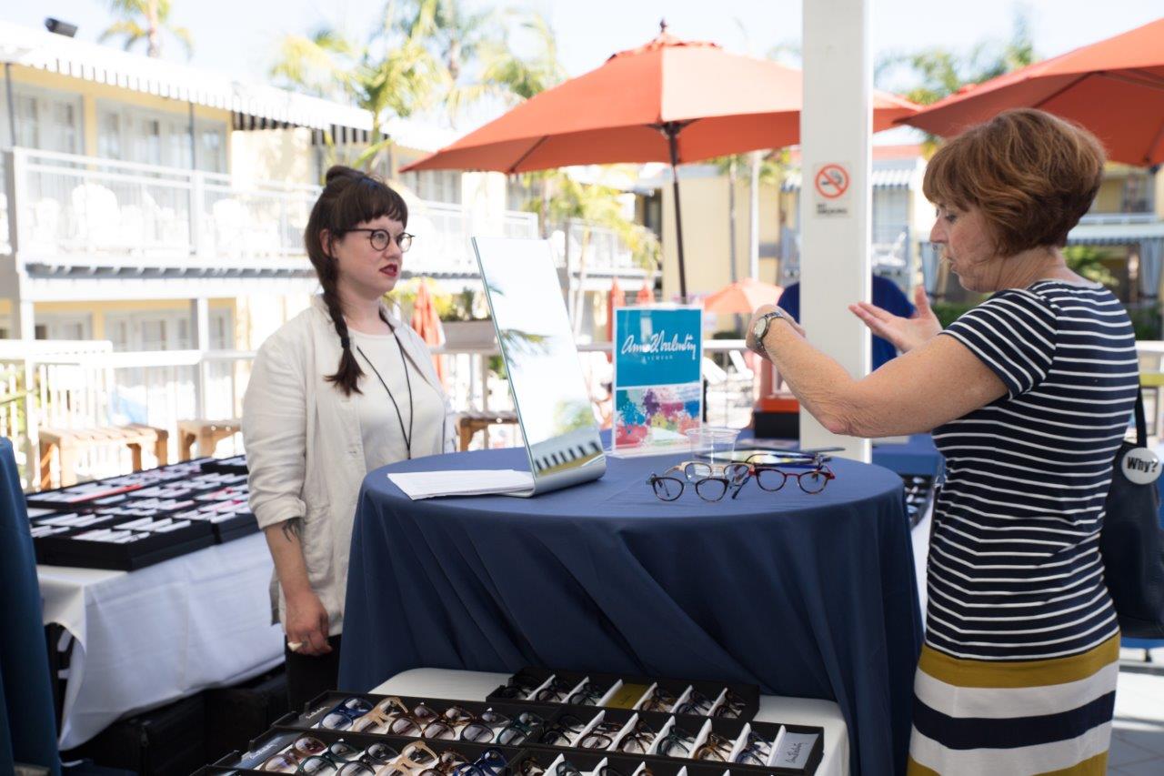 Vendor standing behind her tabletop display chatting with attendee at Raise Your Glasses 2018 Event