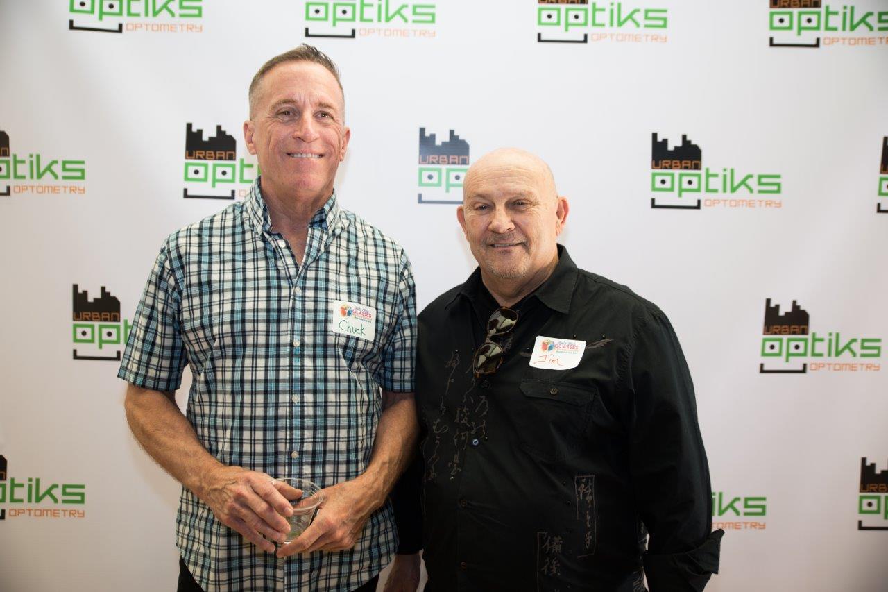 2 guests posing in front of Urban Optiks Optometry banner at Raise Your Glasses 2018 Event