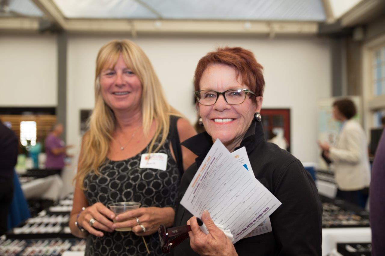 1 person holding a drink and 1 person holding event booklet at Raise Your Glasses 2018 Event