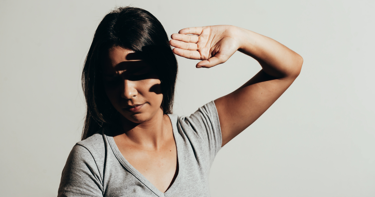 A woman is covering her face with her left hand to shield a bright light.