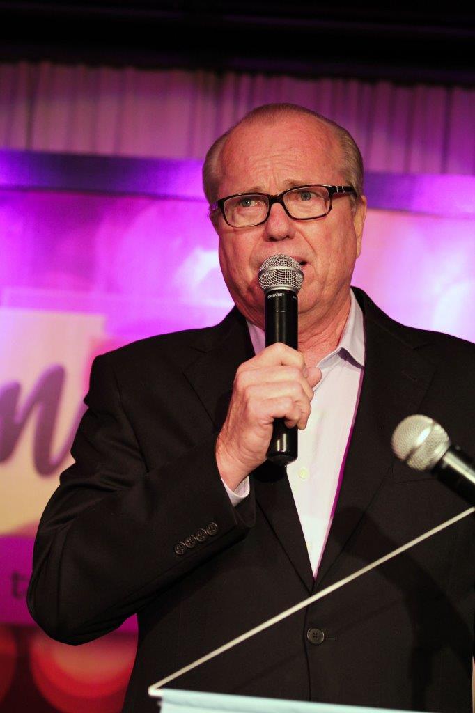 Man talking on microphone at Raise Your Glasses event