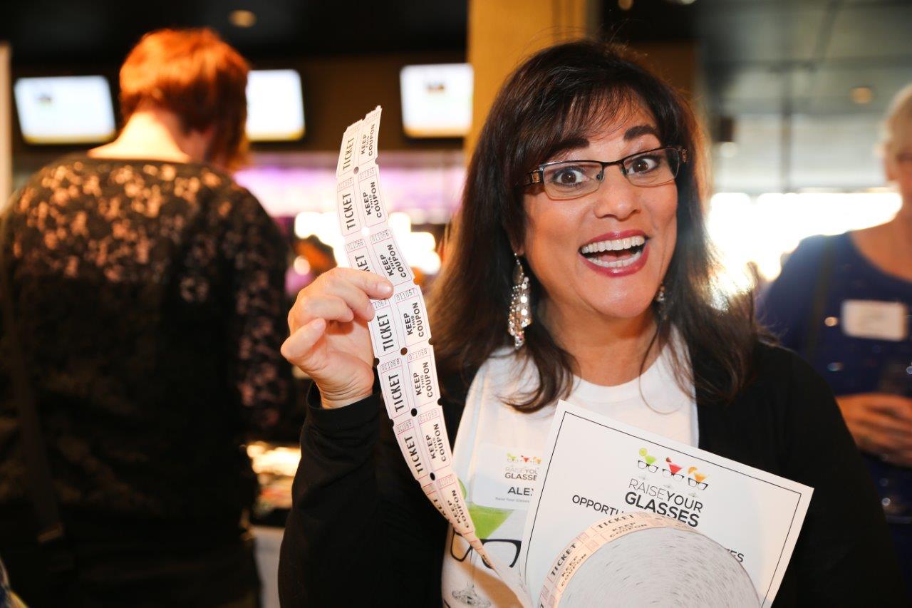 Woman smiling while holding tickets at Raise Your Glasses event