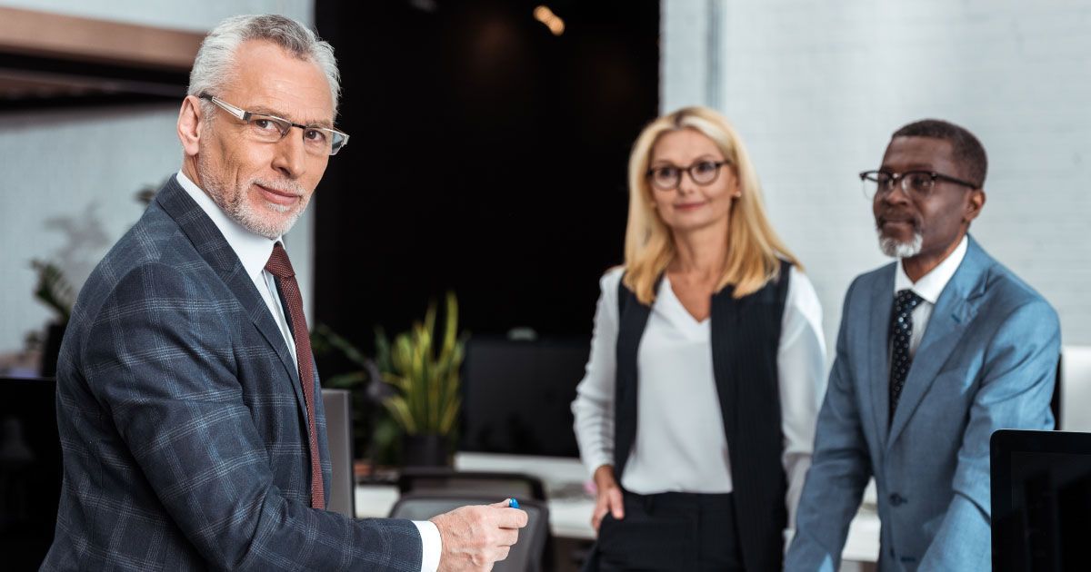 A group of business people wearing glasses are standing next to each other in an office.