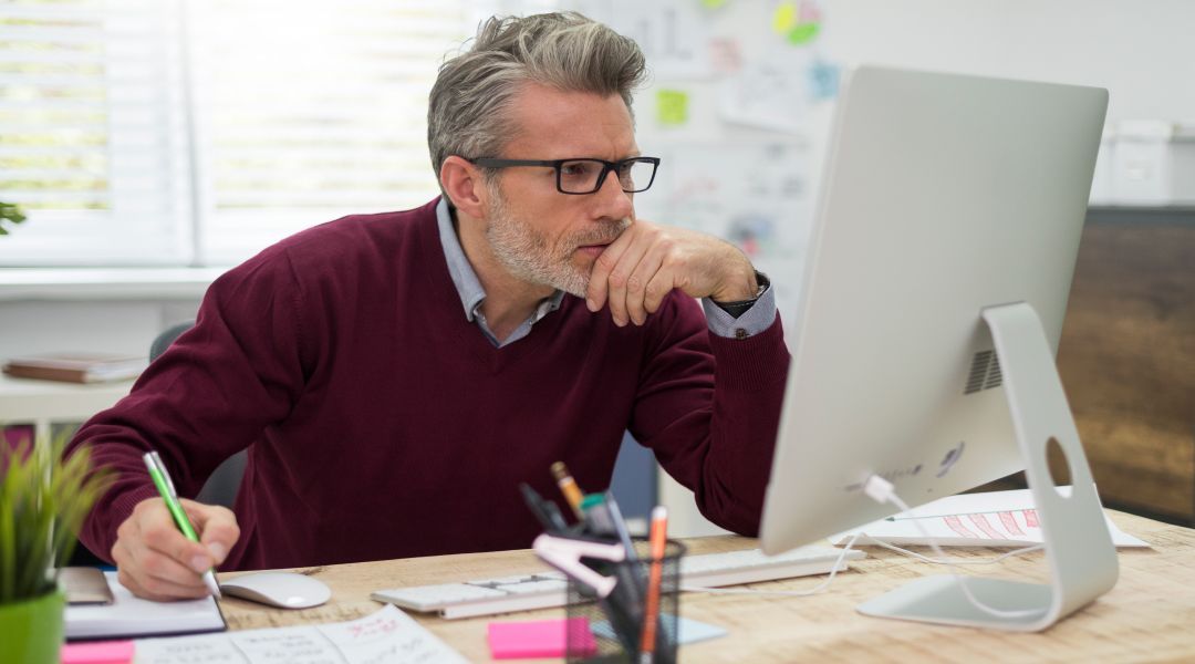 Man in glasses at a desk looking at a computer monitor